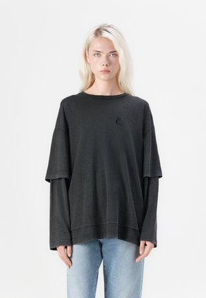 T-shirt oversize nera con scollatura rotonda, maniche corte e maniche lunghe a strati. Presenta un piccolo logo ricamato a forma di barca a vela.