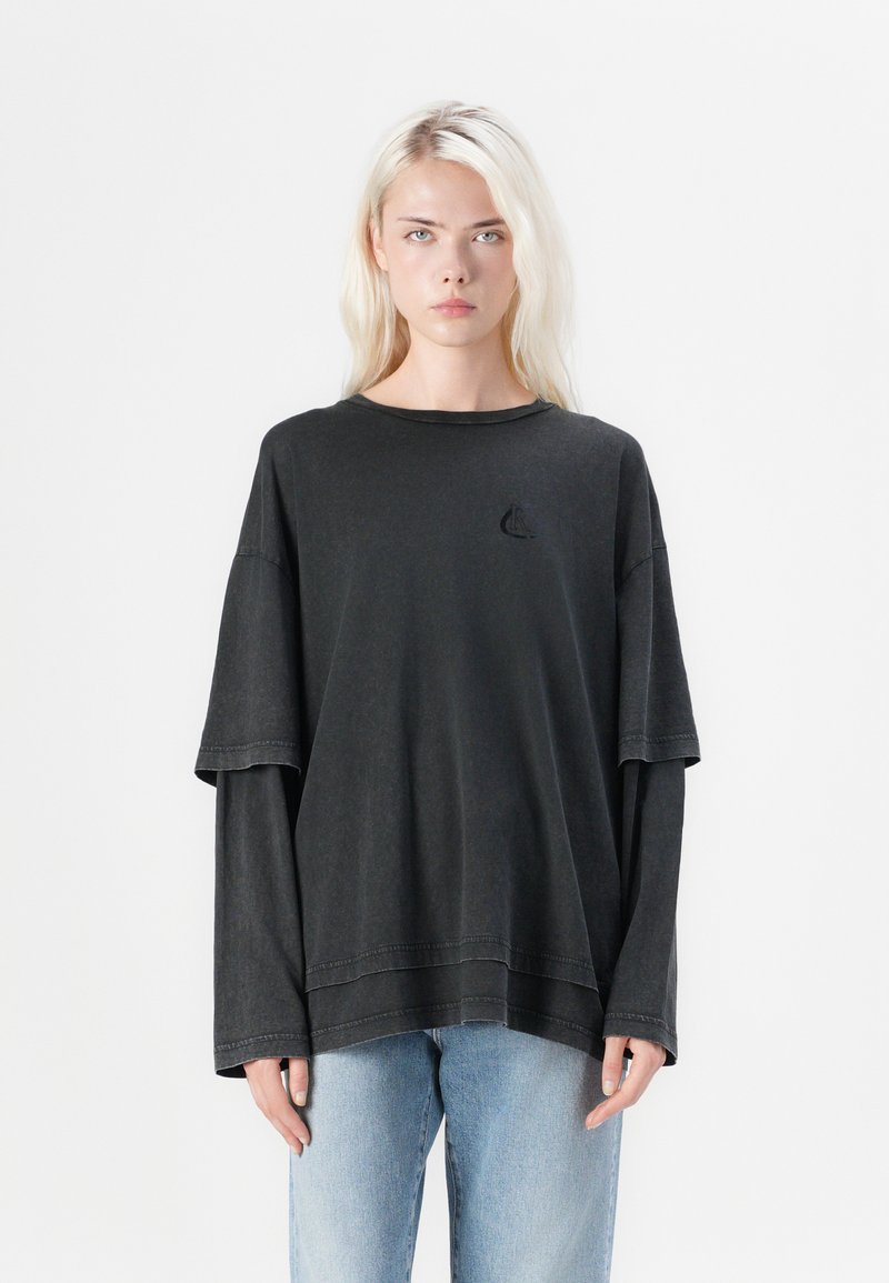 Zwarte oversized t-shirt met een ronde halslijn, korte mouwen en gelaagde lange mouwen. Kenmerkt zich door een klein geborduurd zeilbootlogo.