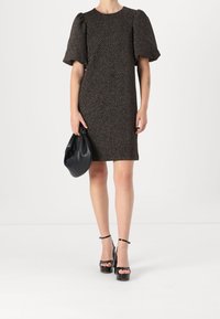 Virkat klänning med korta puffärmar i ett mörkt mönster, kombinerad med en svart axelväska och svarta högklackade plattformsskor. Slät textur.