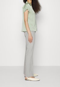 Ljust grön blus med krage och korta ärmar, kombinerad med ljusgrå skräddarsydda byxor och krämfärgade platta skor. Tyget verkar mjukt och lätt.