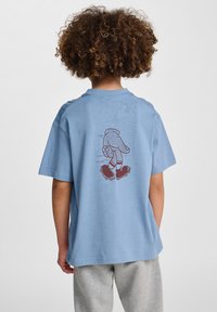 Jasnoniebieska bawełniana koszulka z krótkim rękawem, z czerwoną grafiką przedstawiającą rękę na rolkach nadrukowaną na plecach.