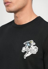 Schwarzes Baumwoll-T-Shirt mit einer farbigen Engelgrafik und einem Banner mit der Aufschrift "fiorucci." Rundhalsausschnitt und strukturierter Stoff.