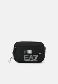 Černá nylonová taška se zipovým uzávěrem, na přední straně s bílým grafickým textem "EA7 EMPORIO ARMANI" a pruhovaným designem. Hladký povrch.