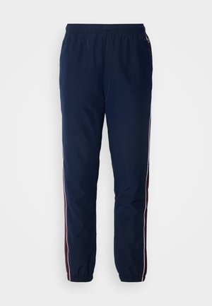 Pantaloni a vento blu navy con elastico in vita e polsini. Presentano strisce laterali bianche e granata. Tessuto morbido e leggero.
