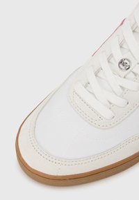 Άσπρο αθλητικό παπούτσι με επάνω μέρος από λείο δέρμα και σουέντ λεπτομέρειες, σόλα από καουτσούκ και στρογγυλά κορδόνια. Ροζ λεπτομέρεια στο πλάι προσθέτει αντίθεση.