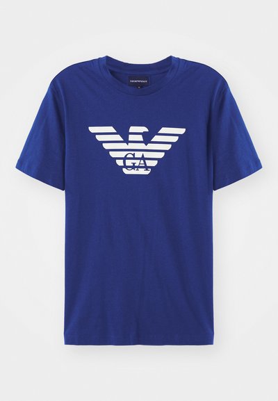 Mėlynas medvilninis marškinėliai su trumpomis rankovėmis, kuriuose yra baltas erelio logotipas ir horizontalių juostų dizainas krūtinėje. Apvalaus kaklo modelis.