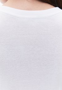 Camicia bianca di cotone con una superficie liscia e leggermente strutturata e un colletto a girocollo a costine, che presenta un design semplice e pulito.