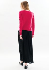 Maglione aderente rosa con maniche lunghe, texture morbida, abbinato a una maxi gonna plissettata nera. L'outfit è completato da ballerine nere.