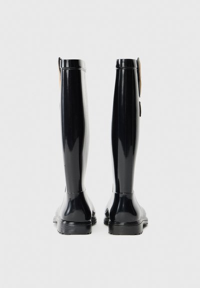 Bottes de pluie en caoutchouc noires avec un design élégant, une tige haute, une semelle texturée et une languette à l'arrière pour un enfilage facile.