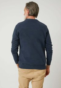 Sudadera azul marino con cuello redondo, puños y dobladillo acanalados, que presenta una textura suave y un detalle en la parte posterior, combinada con pantalones beiges.