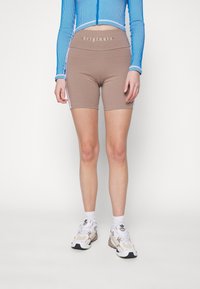 Bruna cykelshorts med hög midja som har ordet "originals" i silvertext, i kombination med vita och bruna sneakers.