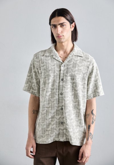 Chemise à manches courtes à boutons en beige clair avec un motif géométrique texturé, dotée d'un col et de cinq boutons sur le devant.
