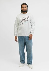 Szara bluza z napisem "Jack & Jones", w połączeniu z jasnoniebieskimi dżinsami. Posiada ściągacze, luźny krój i białe trampki.