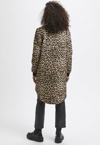 Lang leopardmønstret frakke med sorte manchetter og krave, lavet af textureret stof. Sættes sammen med sorte faux læderbukser og kraftige støvler.