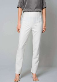 White tailored trousers with a high waist, front pleats, and slim fit. Material is smooth with a slight sheen. Clear block heels visible.
