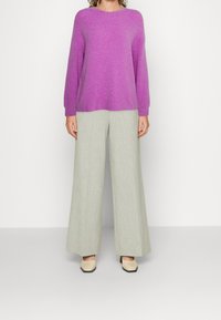 Maglione viola in maglia pelosa con maniche lunghe e scollatura rotonda, abbinato a pantaloni larghi grigi chiari e scarpe con tacco a blocco beige.