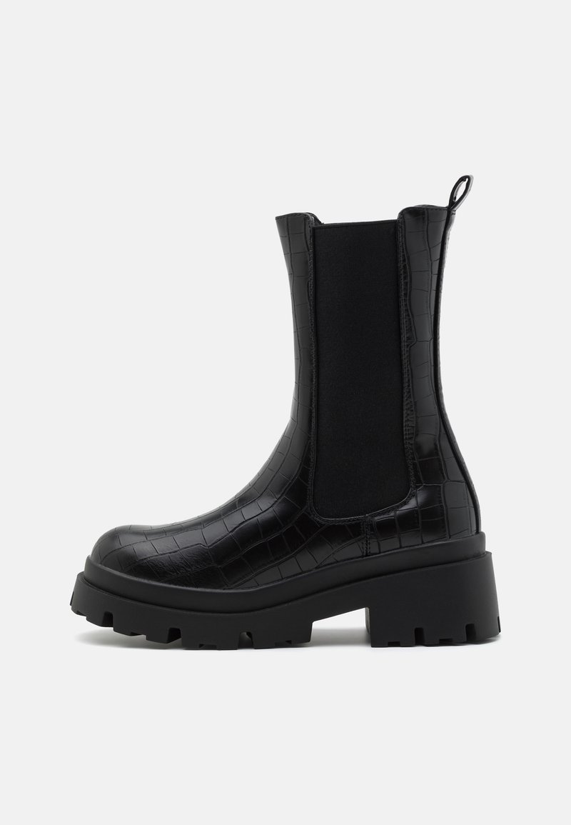 Bottes noires synthétiques à cheville avec une texture crocodile, des panneaux latéraux élastiques, une semelle noire épaisse et une languette à l'arrière.
