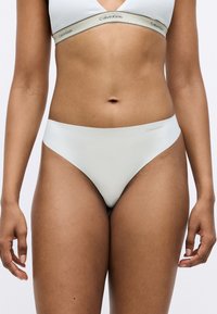 Gaiši pelēks Calvin Klein stringi ar gludu, elastīgu audumu. Iezīmē minimālistisku dizainu un subtile logo uz jostas.