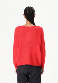 Pull en maille rouge avec une coupe ample, un col rond et des épaules tombantes. Texture douce, ourlet droit et léger éclat.