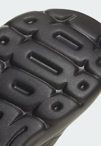 Suola in gomma nera con motivi testurizzati e sollevati e scanalature profonde per una buona aderenza, con un profilo del bordo liscio.