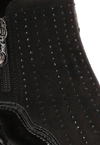 Bota de ante negra con pequeños remaches redondos, ribete de charol brillante y una cremallera plateada en el lateral.