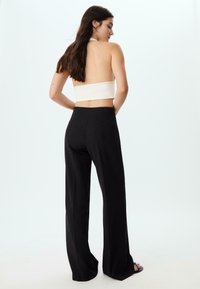 Bela halter crop majica z odprtim hrbtom, v kombinaciji z visokim črnim širokim hlačami. Gladek material, minimalistična zasnova, brez vidnih vzorcev.