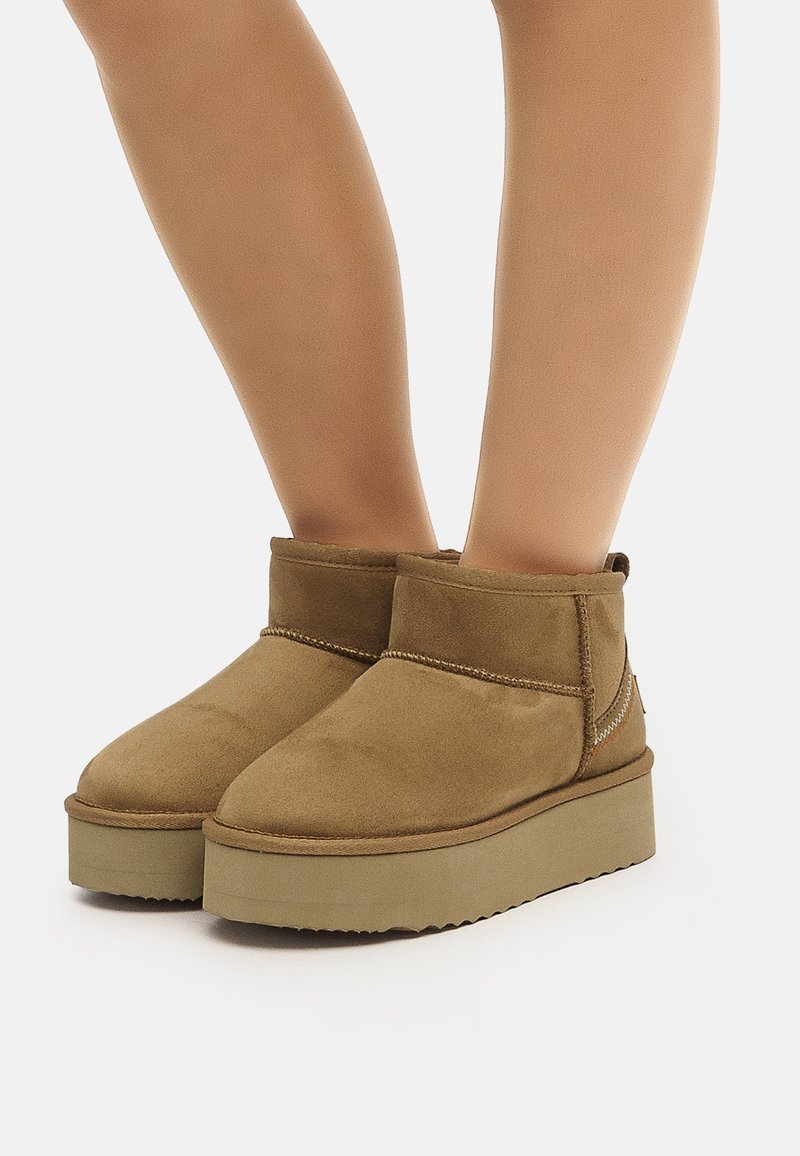 Bottines en daim marron à bout rond, tige courte, et semelle compensée texturée, avec un design simple à coutures autour de la partie supérieure.