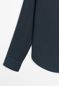 Granatowy rękaw koszuli z długim rękawem, z mankietem i zakrzywionym dołem na białym tle.