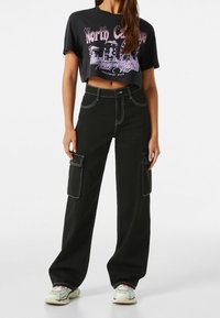 Svarta cargobyxor med vida ben, två sidofickor och kontrasterande vita sömmar. Matchas med en kort grafisk T-shirt.