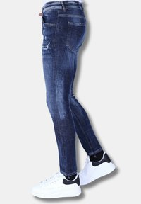 Skinny jeans in donkerblauwe denim met vervaagde accenten en versleten details. Gekocht met witte sneakers met een zwart hielaccent.