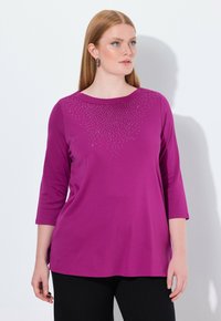 Magenta longsleeve shirt met een ronde halslijn, versierd met een verloop van kleine rhinestones op de borst. Zachte stof en een losse pasvorm.