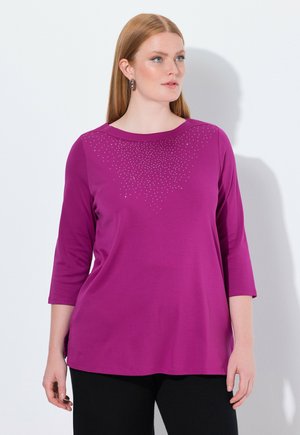 Magenta langærmet skjorte med rund halsudskæring, der har en gradient af små rhinsten ved brystet. Blødt stof og afslappet pasform.