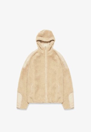 Beżowa kurtka z kapturem, z pluszowym, teksturowanym polarowym ciałem, gładkimi beżowymi akcentami na ramionach i bocznymi kieszeniami. Zamek błyskawiczny na całej długości.