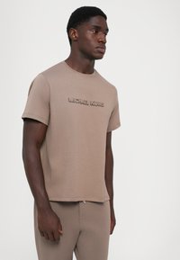 Beige kortermet T-skjorte med preget "MICHAEL KORS"-logo på brystet, rund hals og avslappet passform. Glatt bomullsblandingsstoff.