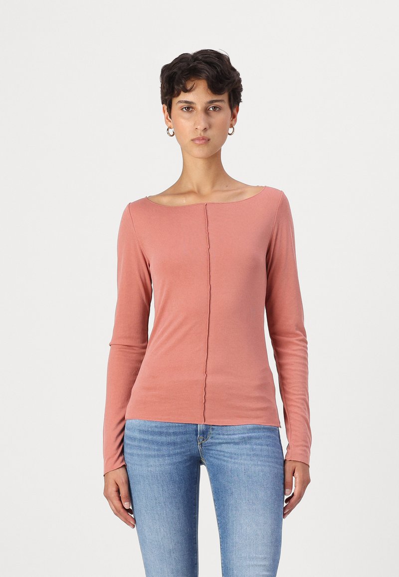 Haut à manches longues de couleur rose pâle en tissu doux, avec un décolleté large et un détail de couture à l'avant, associé à un jean bleu clair.