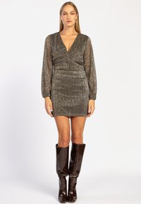 Robe mini scintillante argentée avec un décolleté en V, de longues manches bouffantes et un design froncé. Associée à des bottes brillantes marron jusqu'aux genoux.