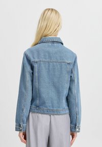 Chaqueta de mezclilla azul claro con collar clásico, puños con botones y detalles en las costuras. Tejido duradero con un acabado ligeramente texturizado.