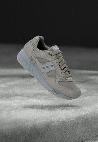 Grauer Sportschuh aus Wildleder und Mesh-Materialien, runde Zehenpartie, Schnürverschluss vorne und hellblaue Akzente an der Seite und Sohle.