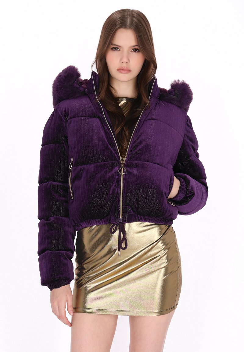 Fioletowa welurowa kurtka puchowa o skrojonym kroju, z zapięciem na zamek i kapturem wykończonym futrem. Połączona z błyszczącą złotą mini spódnicą.