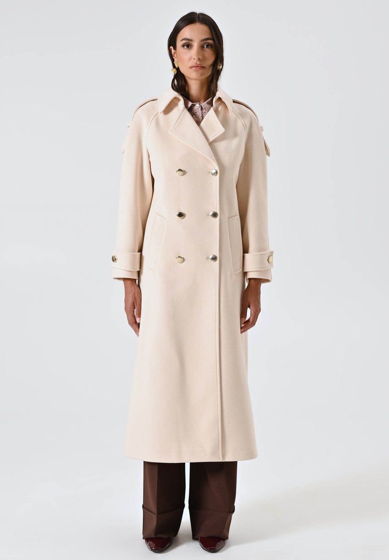 Cappotto di lana beige a doppio petto con grandi bottoni dorati, tasche laterali e spalline; silhouette lunga e dritta con una finitura pulita.