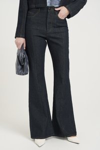 Temno denim flare kavbojke s kontrastnim šivi, visokim pasom in gladko teksturo. V kombinaciji z belimi špicastimi petami in sivo torbico.