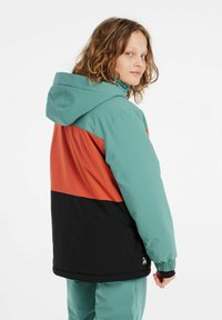 Giacca color block con parte superiore in teal, sezione centrale arancione e parte inferiore nera. Realizzata in tessuto liscio e texture, con cappuccio regolabile.