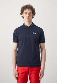 Navy polo shirt with a textured collar, featuring three buttons and a small logo on the chest. Short sleeves and a fitted design.