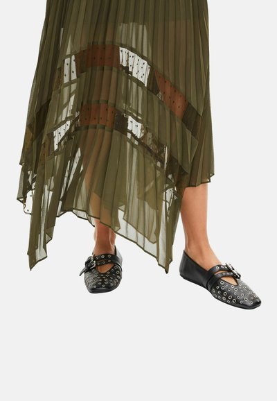 Legs wearing black flat shoes with silver eyelets and buckles, under an olive green sheer pleated skirt with patterned panels.