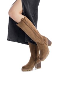 Stivali al ginocchio in suede marrone con tacco spesso e suola testurizzata, dotati di zip laterale e cuciture decorative lungo i bordi.