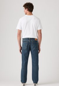 Blauwe spijkerbroek met een straight leg pasvorm, vijf zakken en een bruine leren merkpatch. Draag het met een wit T-shirt met ronde hals.