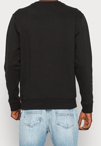 Sudadera negra con cuello redondo y puños acanalados, fabricada con un tejido suave. Presenta un dobladillo recto y costuras planas. Se lleva con jeans de color azul claro.