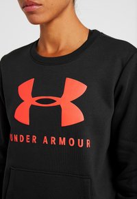 Felpa nera con colletto rotondo, caratterizzata da un prominente logo rosso Under Armour e testo sulla parte anteriore, realizzata in tessuto testurizzato.