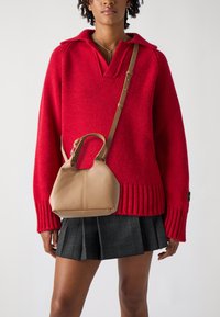 Rød strikket sweater med krave, ribbet kant, parret med en lille beige lædertaske. Sort skotsk ternet plisseret nederdel og skulderrem på tasken.