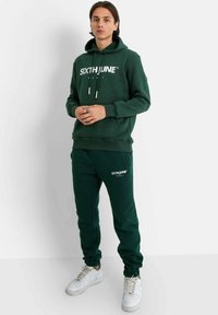 Sudadera verde y pantalones de chándal a juego con el logo "SIXTH JUNE PARIS" en blanco. Corte casual con cordones y puños acanalados.